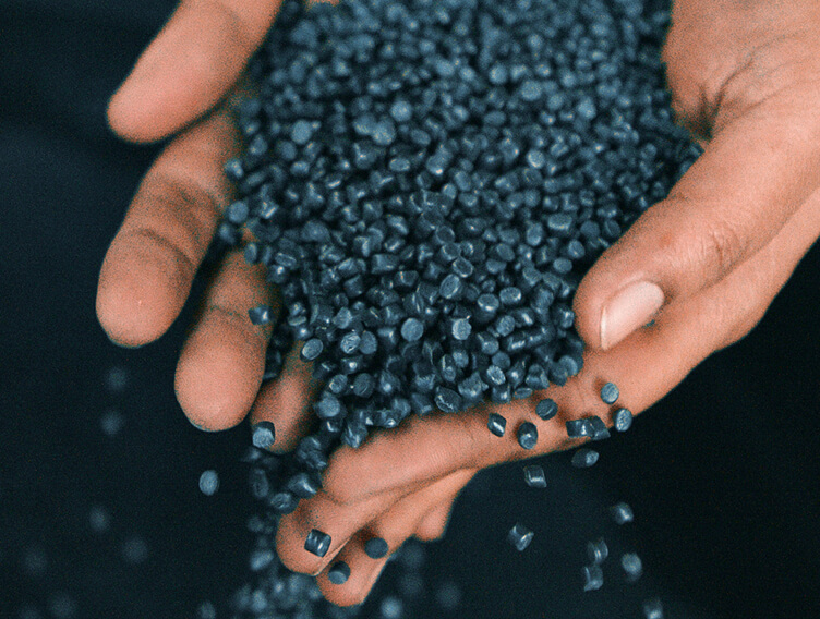Two hands hold dark blue plastic granules as individual pellets fall between the fingers.