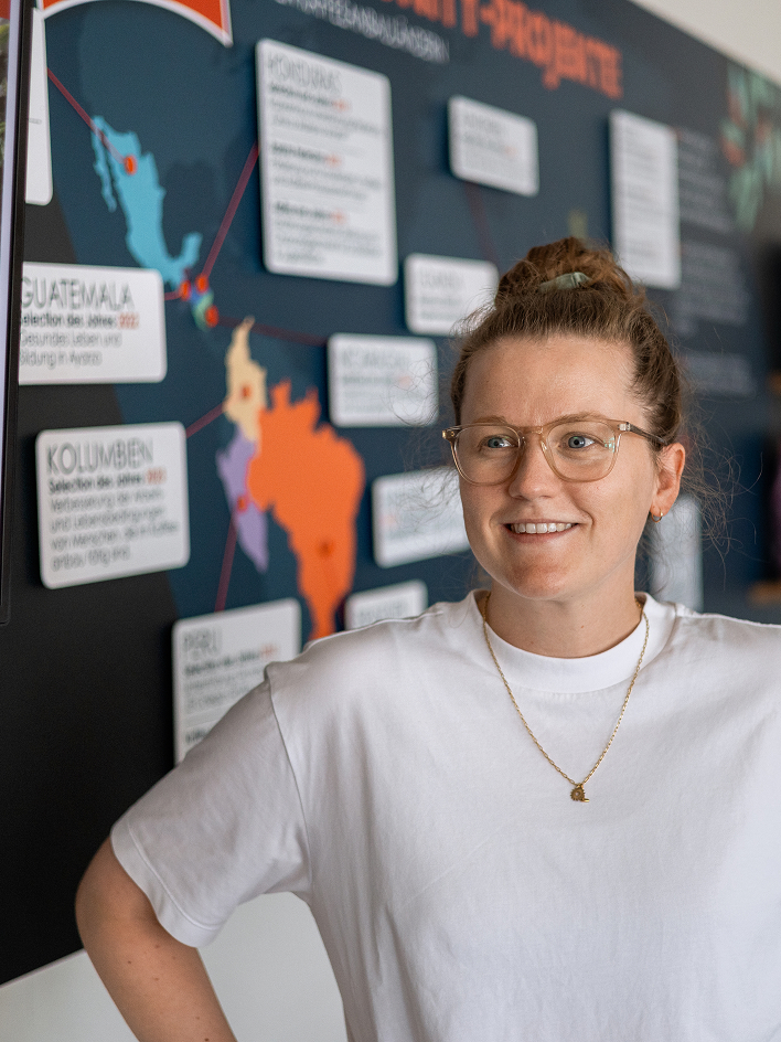 Protagonist in glasses stands before a world map of projects in coffee-growing countries.
