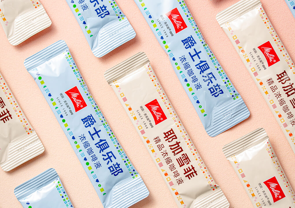 Close up of assorted Melitta Coffeeliquid sticks with Chinese lettering and red Melitta logo arranged on pastel pink background.