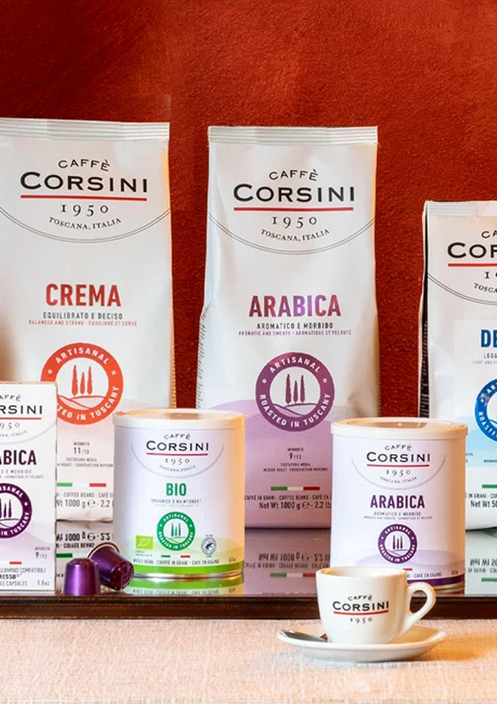 Wide Caff&egrave; Corsini product range with beans, capsules and tins in multiple blends arranged against terracotta backdrop.