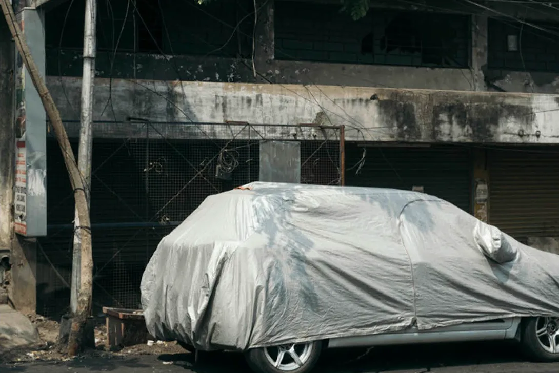 Ein verfallenes Haus, davor steht ein abgedecktes Auto (Foto)