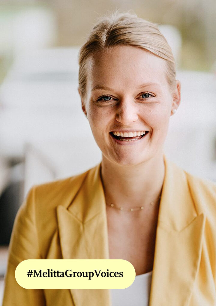 Portr&auml;t einer l&auml;chelnden Mitarbeiterin im gelben Blazer, unten gelbes Hashtag Banner &bdquo;#MelittaGroupVoices&ldquo;.
